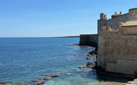 Alte Steingebäude von Ortigia ragen unter blauem Himmel direkt aus dem klaren blauen Meer