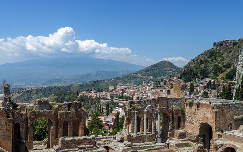 Ziegelruinen des antiken Theaters von Taormina unter blauem Himmel, dahinter Stadt, Küste und Ätna