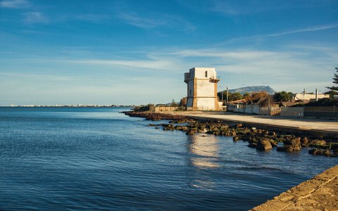 Alter Steinturm an Trapanis Küste am Ende eines felsigen Wellenbrechers, ruhiges Meer und weiches Abendlicht