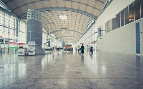 Lange, helle Terminalhalle am Flughafen Alicante mit gewölbtem Dach und wenigen Reisenden