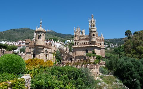 Verzierte Steintürme des Castillo de Colomares über grünen Gärten unter leuchtend blauem Himmel