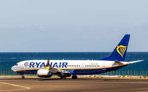 Blau-weißes Verkehrsflugzeug auf der Startbahn des Flughafens Gran Canaria, dahinter das Meer