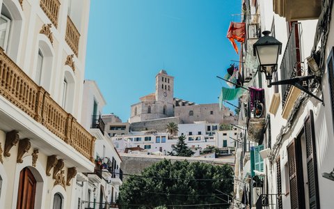 Weiße Häuser in einer Straße von Ibizas Altstadt, darüber der Kathedralenturm auf dem Hügel
