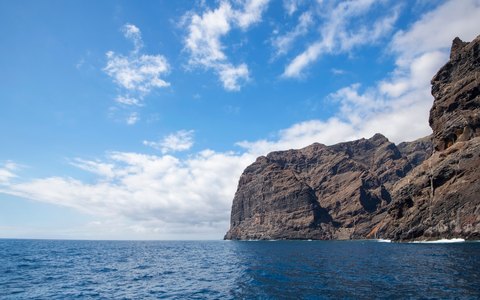Steile dunkle Klippen von Los Gigantes über dem Meer unter strahlend blauem Himmel mit weißen Wolken