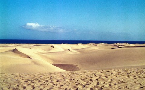 Goldene Sanddünen bis zum fernen blauen Meer unter klarem blauem Himmel mit wenigen Wolken