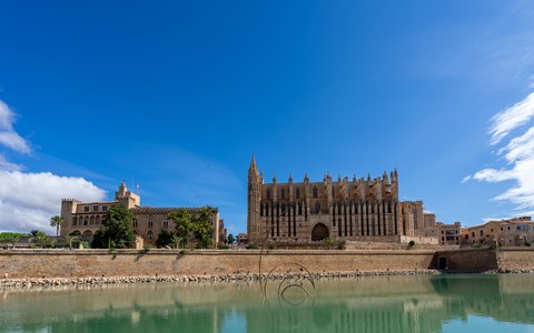 Kathedrale von Palma und Almudaina-Palast über den Ufermauern, gespiegelt in ruhigem Wasser unter blauem Himmel