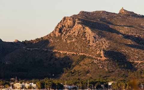 Segelboote auf ruhigem Wasser vor den felsigen Hügeln von Port de Pollença im warmen Abendlicht