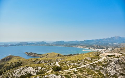 Weiter Blick über die Bucht von Alcúdia mit grünen Landzungen, Küste und Bergen unter klarem blauem Himmel