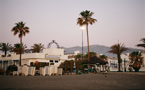 Palmen und eine Strandbar an der Playa Los Alamos in Torremolinos bei Sonnenaufgang, dahinter Berge