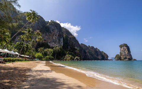 Sandstrand von Ao Nang mit Palmen, Kalksteinfelsen und einem freistehenden Felsturm vor der Küste