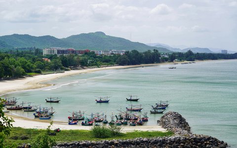 Blick auf die in der Bucht am Strand Khao Tao bei Hua Hin vertäuten Fischerboote mit grünen Hügeln dahinter