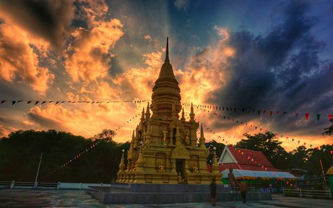 Eine goldene Pagode mit Gebetsfahnen unter einem orangefarbenen und dunkel bewölkten Himmel