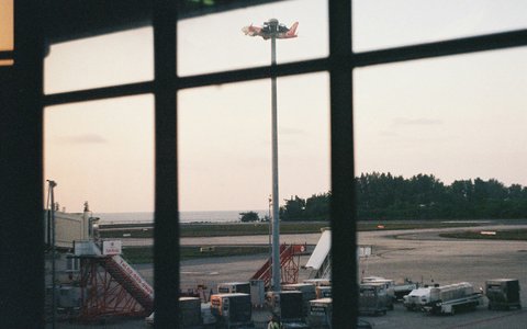 Das Vorfeld am Flughafen Phuket mit Fluggasttreppen und Bodenfahrzeugen, durch ein Terminalfenster gesehen