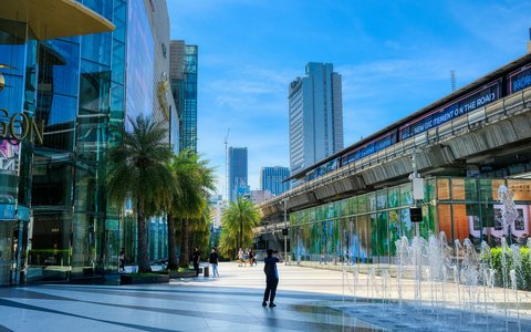 Blick auf die Glasfront des Siam Paragon neben der Hochbahn und einem Brunnenplatz in Bangkok