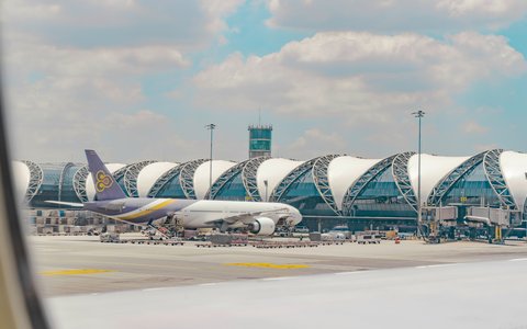 Verkehrsflugzeug von Thai Airways auf dem Vorfeld vor dem geschwungenen Terminaldach und dem Kontrollturm am Flughafen Suvarnabhumi