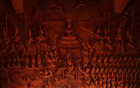 Ein rotes, geschnitztes Wandrelief eines sitzenden Buddha, umgeben von Reihen von Figuren