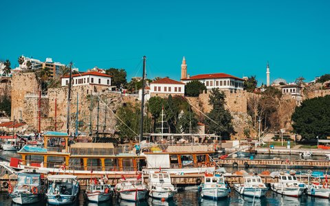 Blick auf die im alten Hafen von Kaleiçi festgemachten Boote unterhalb der Mauern und Häuser mit roten Dächern in Antalyas Altstadt bei blauem Himmel