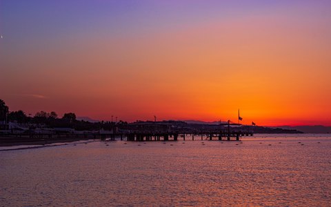 Langer Steg als Silhouette vor einem orange-rosa Sonnenuntergangshimmel über dem Meer