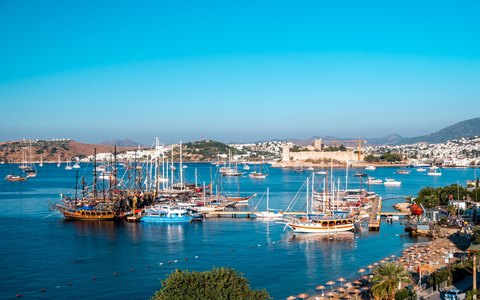 Unter strahlend blauem Himmel liegen Gulets und Segelboote im Yachthafen von Bodrum, mit der Burg von Bodrum auf der anderen Seite der Bucht