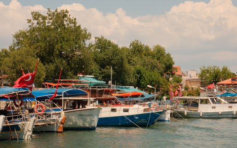 Blick auf bunt bemalte Ausflugsboote mit türkischen Flaggen, die an einem grünen Flussufer liegen