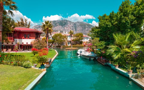 Türkisfarbener Kanal mit Palmen, Villen und vertäuten Booten in Göcek vor Bergen