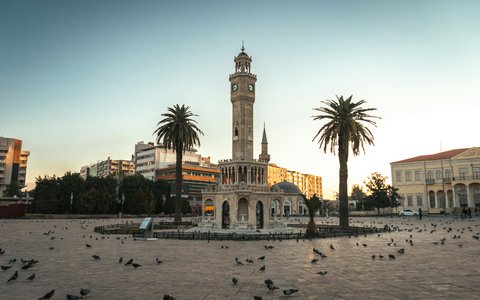 Uhrturm von Izmir zwischen zwei Palmen auf dem Konak-Platz mit Tauben auf dem Pflaster