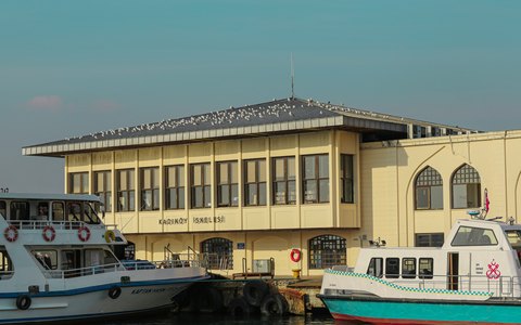 Historisches Gebäude des Fähranlegers Kadıköy mit daneben liegenden Fähren unter blauem Himmel