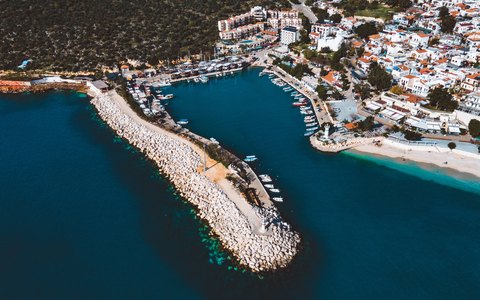 Luftbild von Kalkans Hafenmauer, vertäuten Booten und weißen Häusern neben türkisfarbenem Wasser
