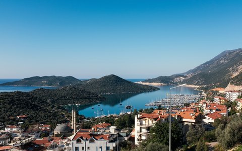 Luftbild des Hafens von Kaş und weißer Häuser mit grünen Hügeln und blauem Meer unter klarem Himmel
