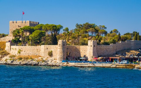 Die steinerne Festung auf der Taubeninsel bei Kuşadası mit türkischer Flagge, Pinien und blauem Wasser unter blauem Himmel