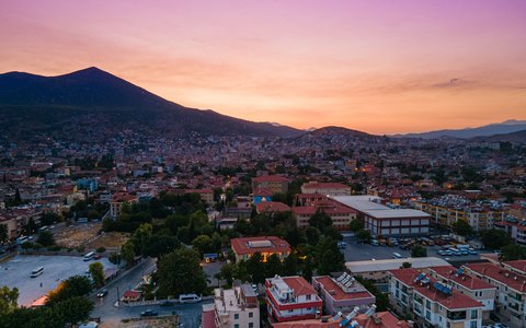 Luftaufnahme der Stadt Milas unterhalb dunkler Berge unter einem rosa und orangefarbenen Sonnenuntergangshimmel