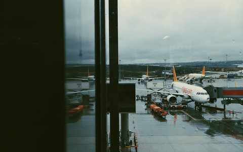 Nasses Vorfeld mit geparkten Verkehrsflugzeugen am Flughafen Sabiha Gökçen, an einem Regentag durch ein Terminalfenster gesehen