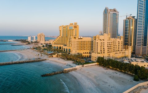 Luftaufnahme von Adschmans Strand sowie den Hotels und Hochhäusern direkt am Meer, bei ruhigem Wasser im Licht des späten Nachmittags