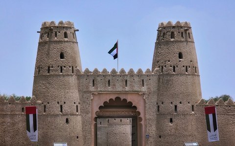 Zwei runde Türme und das Tor des Al Jahili Fort mit der Flagge der VAE unter klarem blauem Himmel
