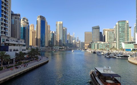 Hochhäuser am Wasser der Dubai Marina mit Jachten und Promenade unter klarem blauem Himmel