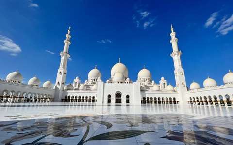 Weiße Kuppeln und hohe Minarette der Scheich-Zayid-Moschee unter klarem tiefblauem Himmel
